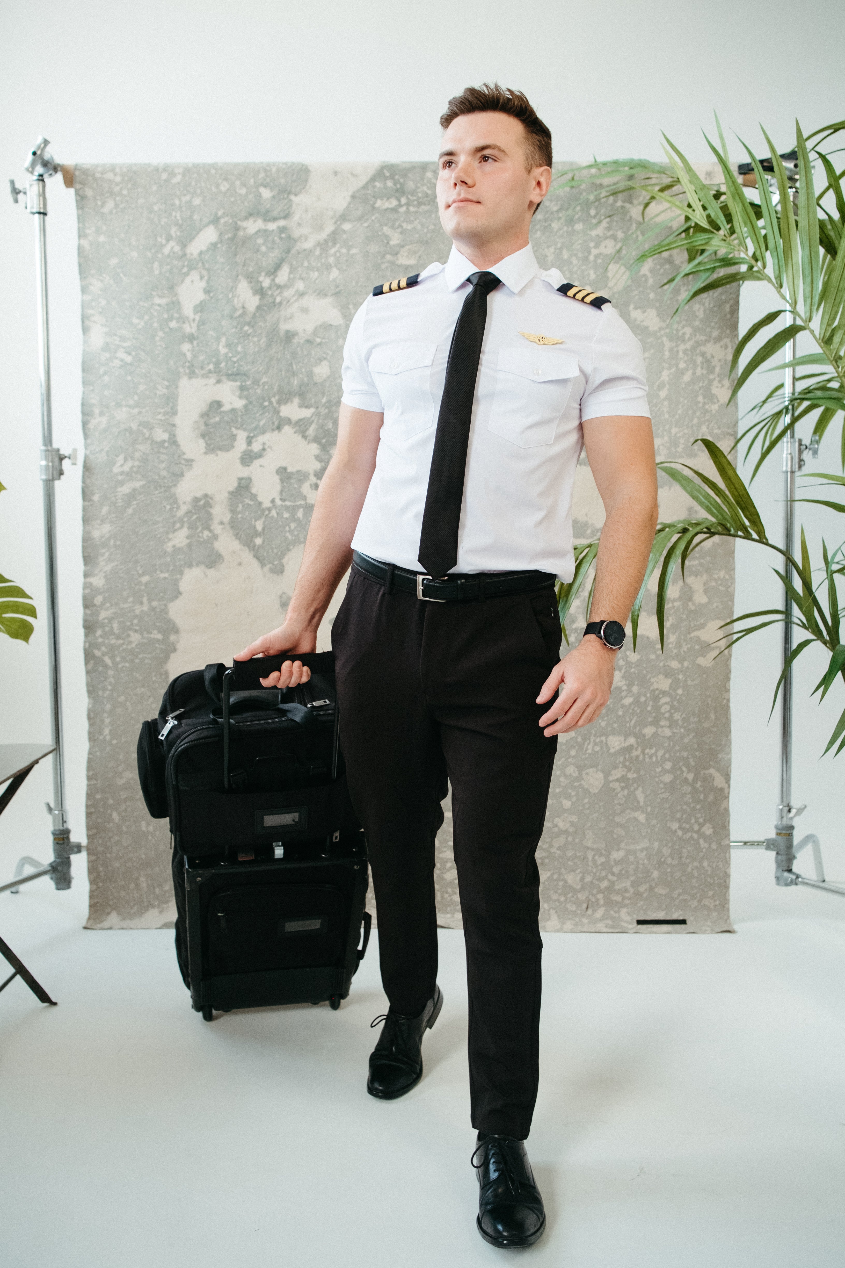 Airline pilot in white short-sleeve Flight pilot shirt with black tie and pilot wings badge, pulling a black rolling flight bag