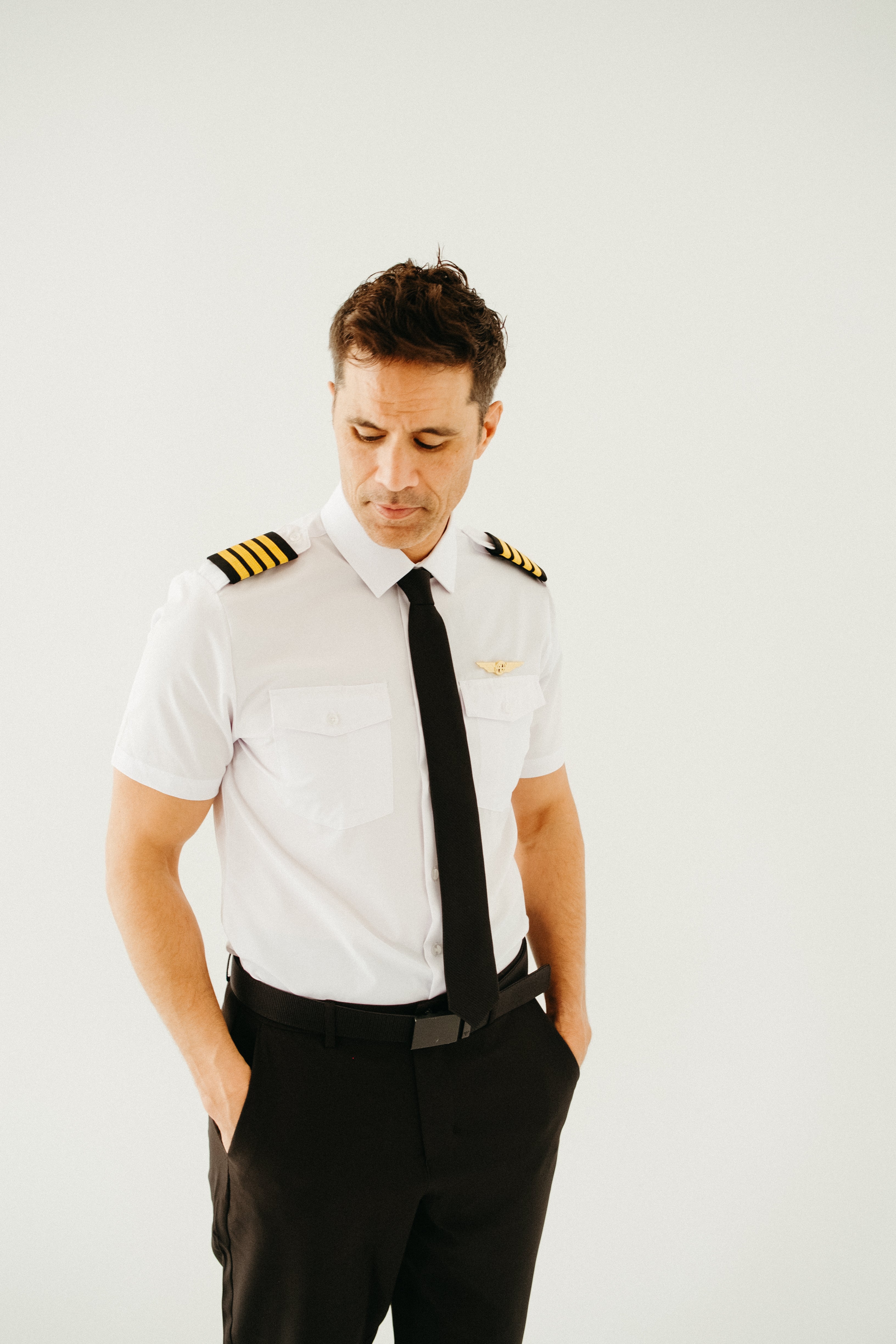 Male airline pilot looking down while wearing a white short-sleeve Flight pilot shirt with four-stripe epaulettes and black tie