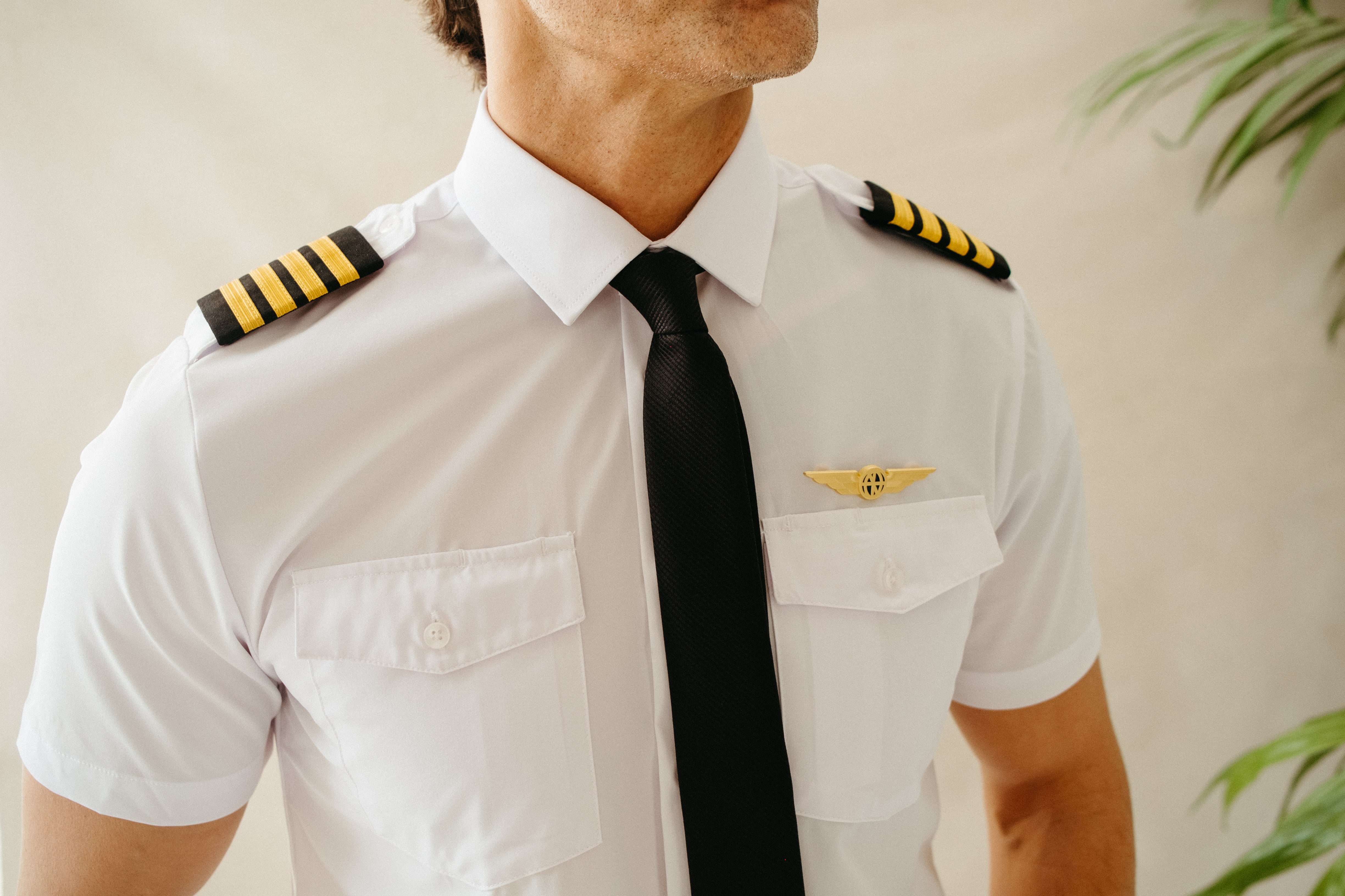 Close-up of a white Flight pilot shirt chest with four-stripe epaulettes, black tie, dual flap pockets, and gold pilot wings badge